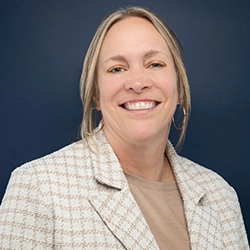 Jenny Miller smiles into the camera against a dark blue background.
